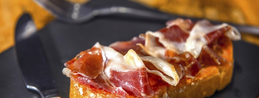 A mouthwatering selection of gourmet montaditos showcasing fresh ingredients like jamón Serrano, Manchego cheese, anchoas, and piquillo peppers, artfully arranged on toasted pan de flauta slices.